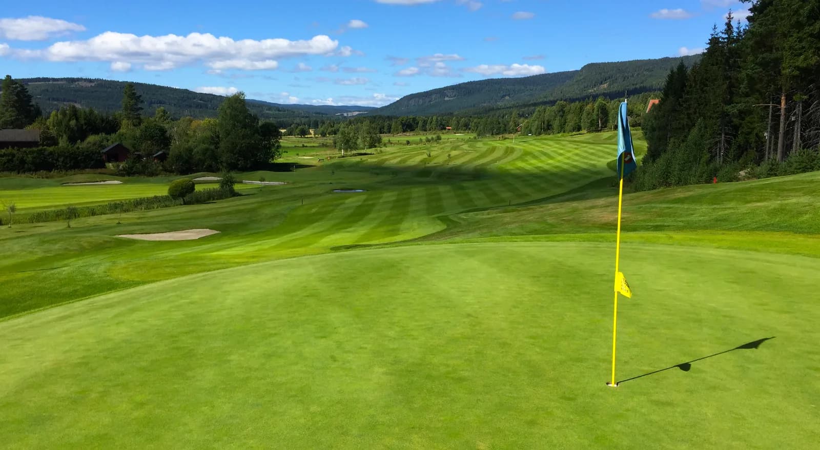 Green on hole 17 at Aas Gaard Golf Park with flag and panoramic view of hills and blue sky