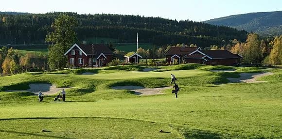Golfers near bunkers on hole 7 at Aas Gaard Golf Park with red farm buildings and hills