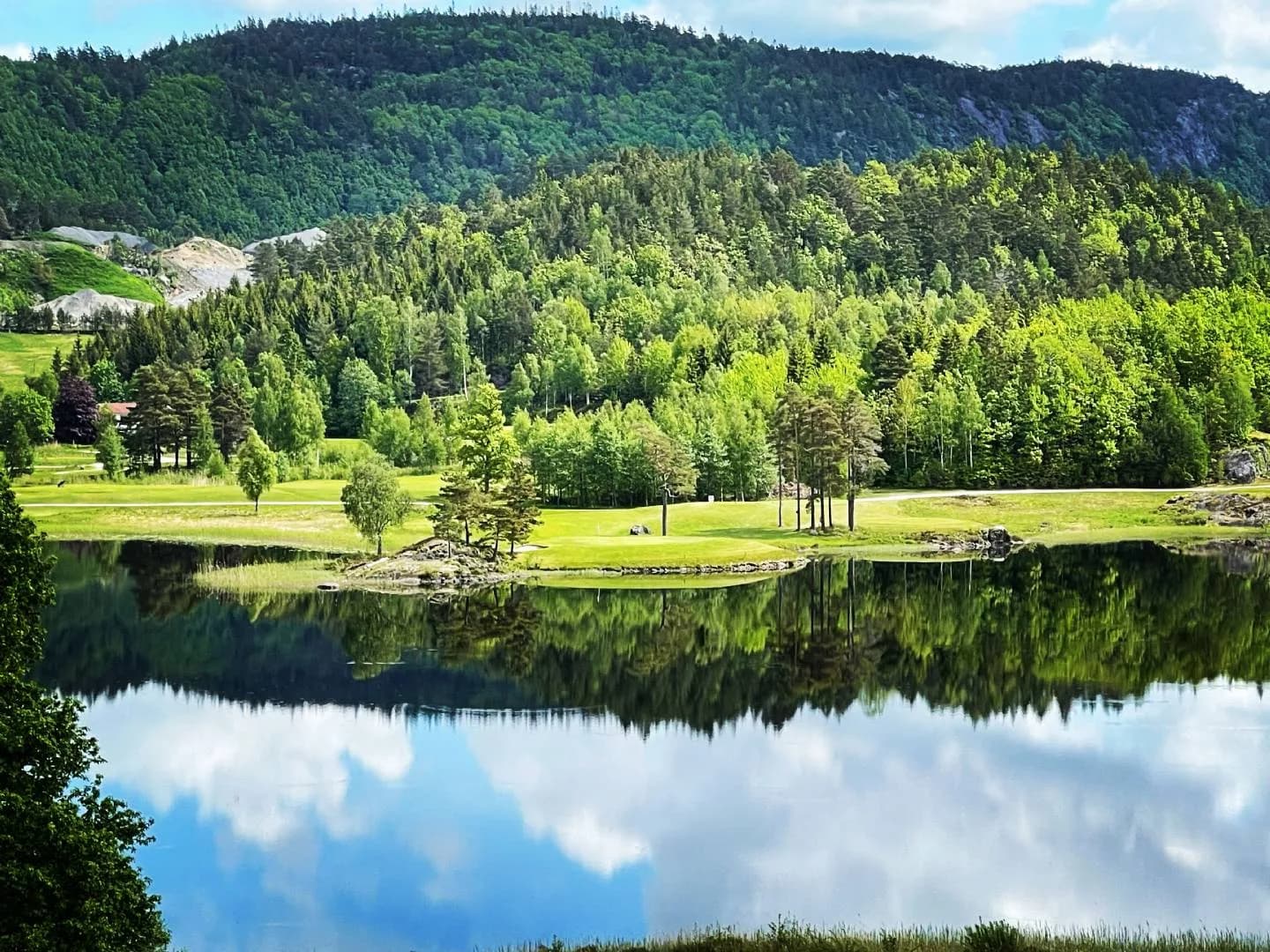 Bjaavann Golf Club with mirror-smooth water reflecting clouds, fairways and forested hills