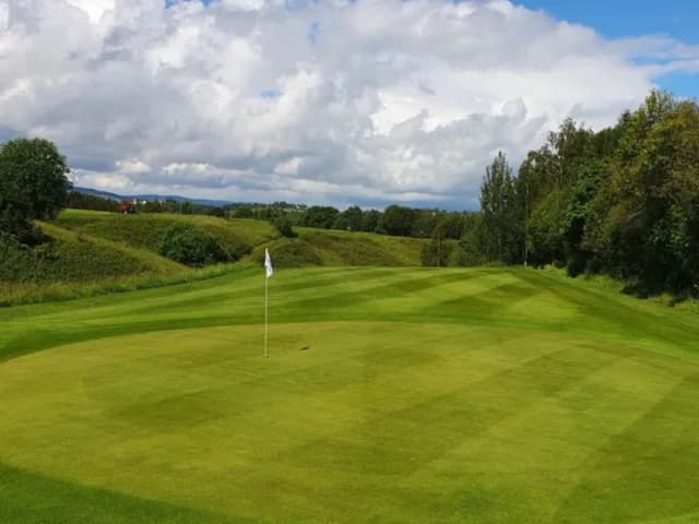 Green with flag on hole 5 at Fet Golf Club with rolling hills in the background
