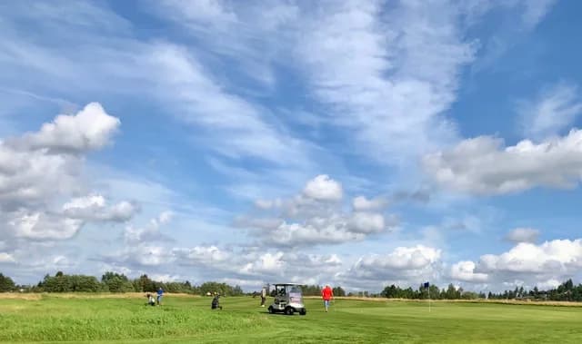Golfers with golf cart on the fairway at Fet Golf Club with wide sky and green landscape