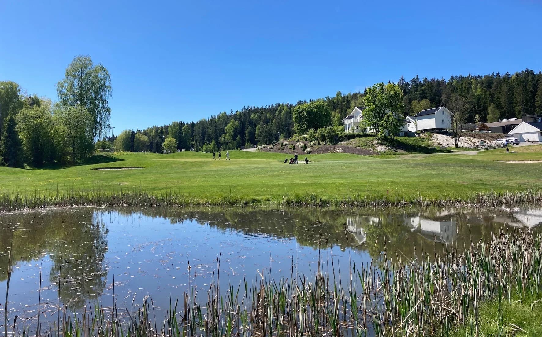 Gjersjøen Golf Club with water hazard, fairway and clubhouse in forest terrain by Lake Gjersjøen
