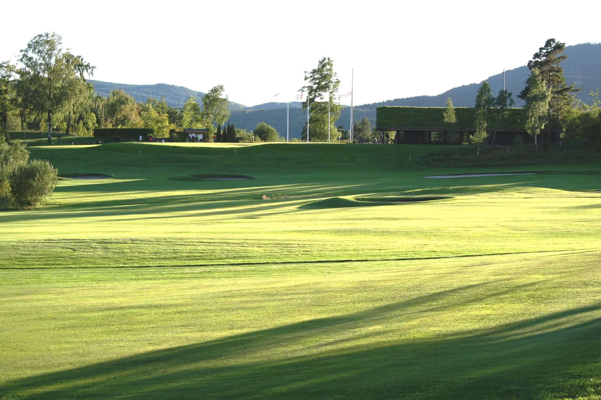 The clubhouse at Grenland & Omegn Golf Club viewed from hole 10 with fairway, greens and mountains in the background