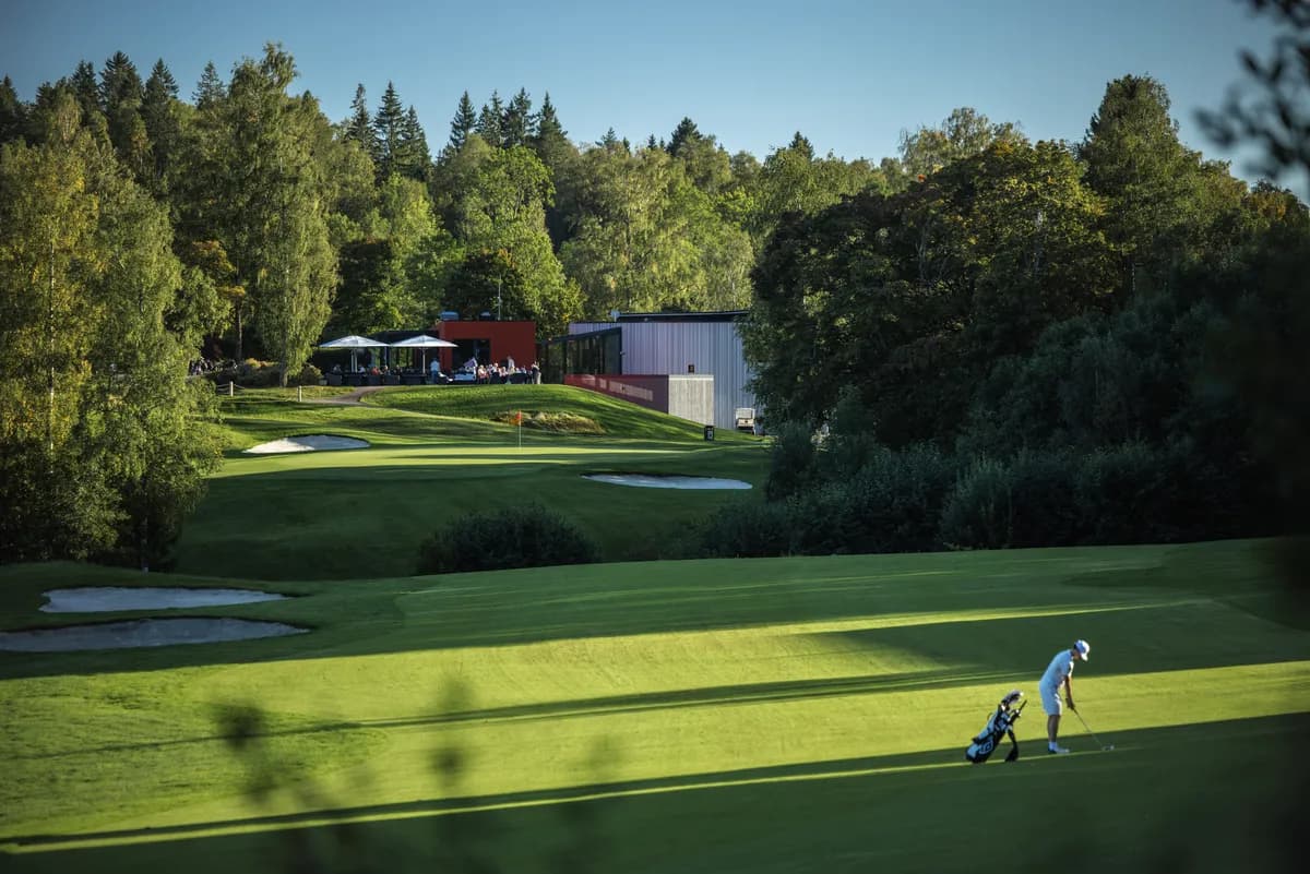 Golfer on fairway at Haga Golf Club with clubhouse, bunkers and forest in the background
