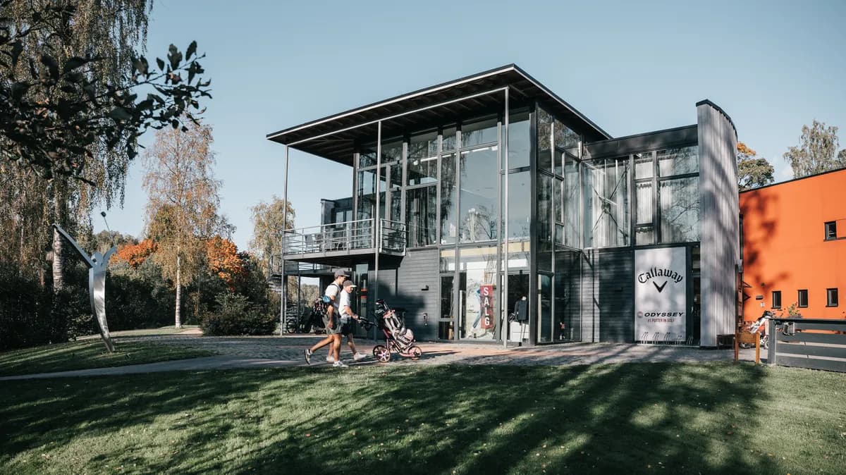 Clubhouse and pro shop at Haga Golf Club with glass facade, sculpture and golfers with trolley in autumn sun