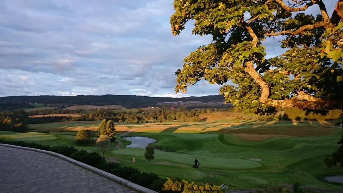 View from the clubhouse at Hauger Golf Club with evening light over fairways, water hazard and hills in the background