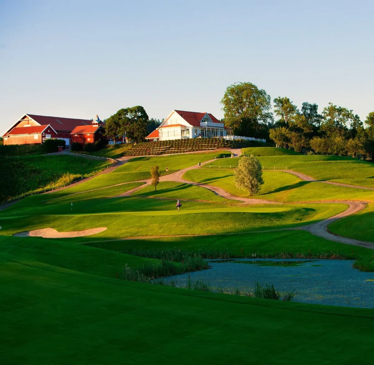 Overview of Hauger Golf Club with clubhouse, bunkers, water hazard and green fairways in evening sunlight at Slattum