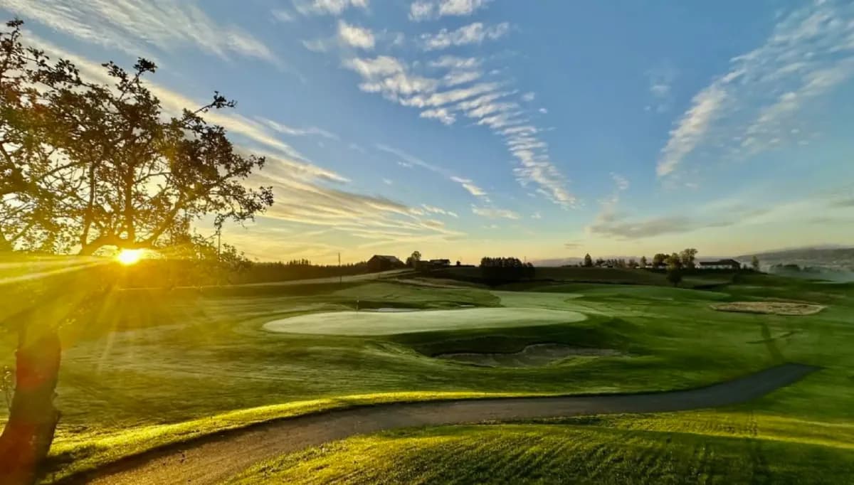 Sunset over green and bunkers at Hauger Golf Club with sunrays and dramatic sky