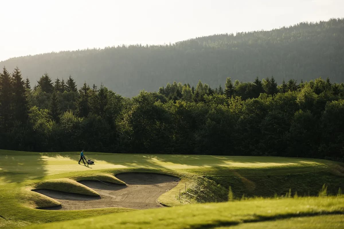 Golfer near bunkers at Holtsmark Golf Club in morning light with forested hills