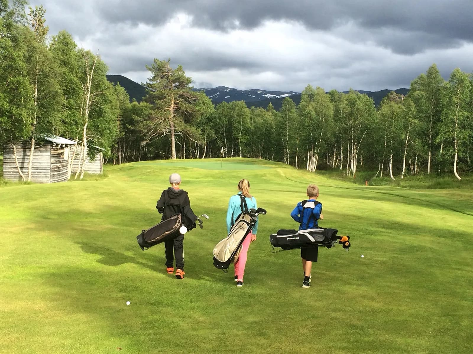 Three junior golfers with bags on hole 3 at Hovden Golf Club with mountains in the background