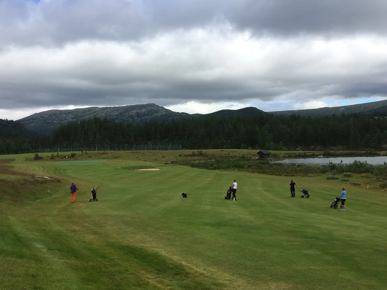 Golfers on hole 5 fairway at Hovden Golf Club with mountain panorama and water