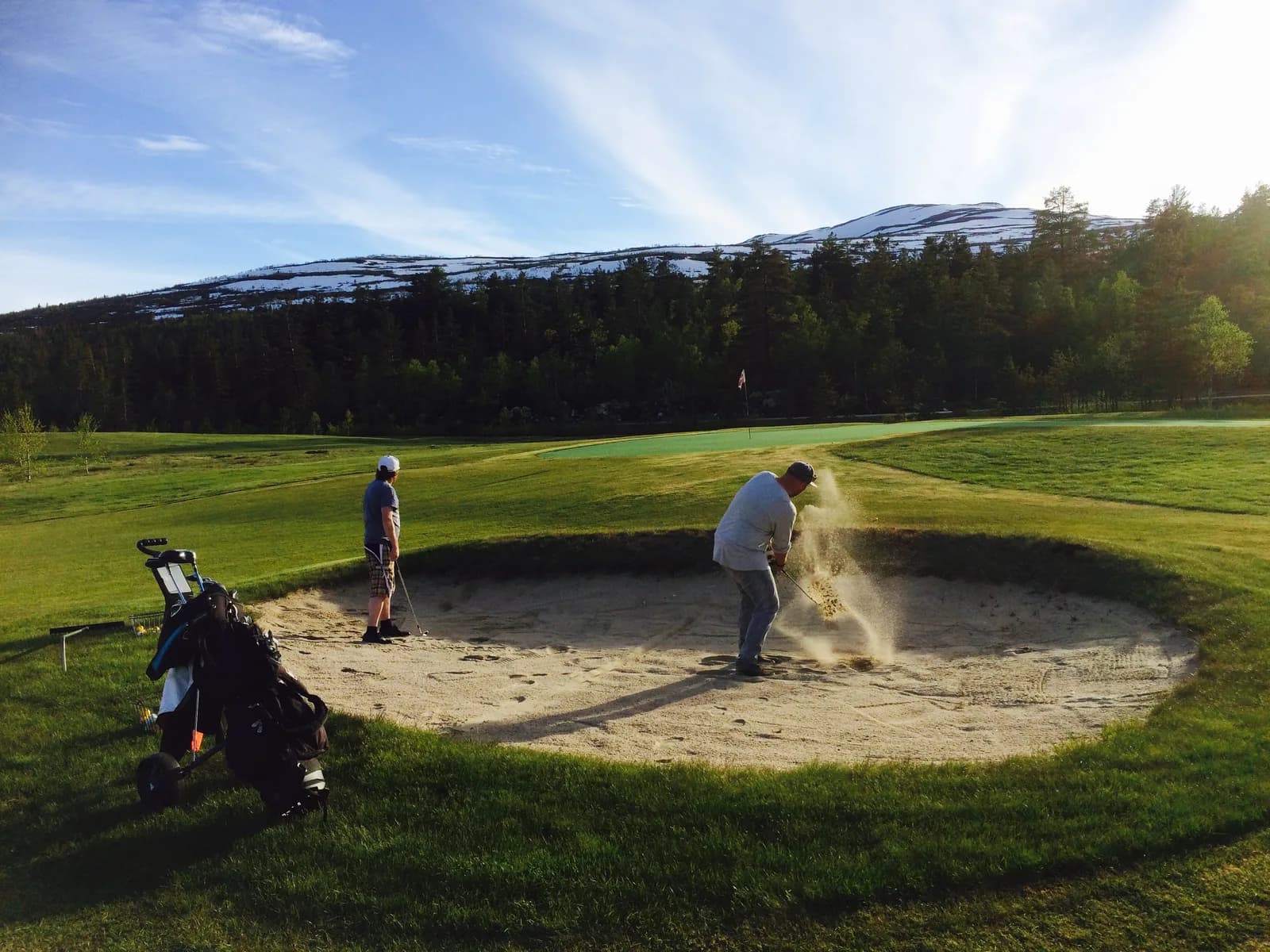 Bunker shot on hole 7 at Hovden Golf Club with snow-capped mountains in the background