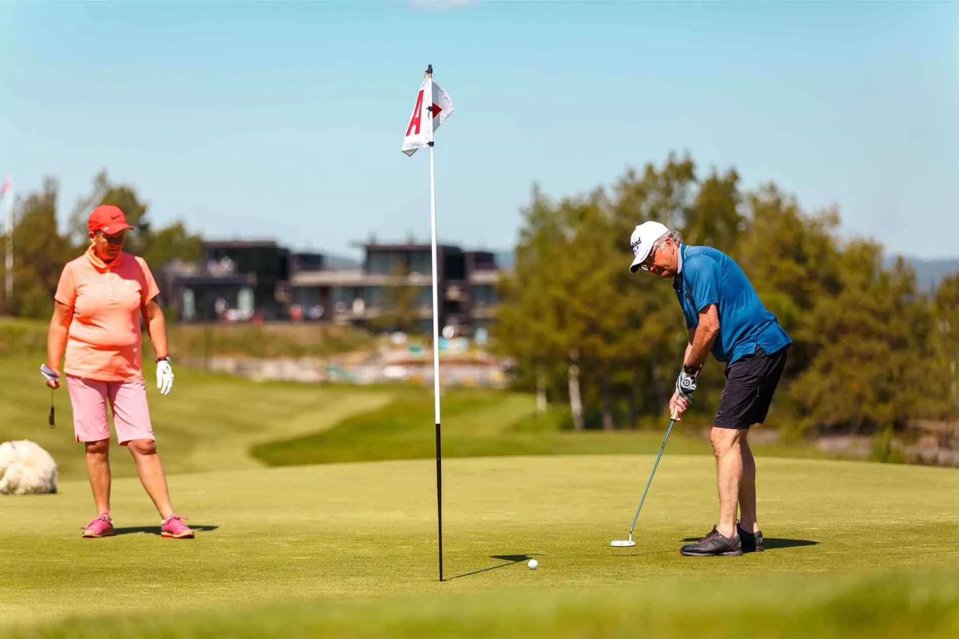Golfer hitting from bunker at Kragerø Golf Club with sand spray and golf course in the background