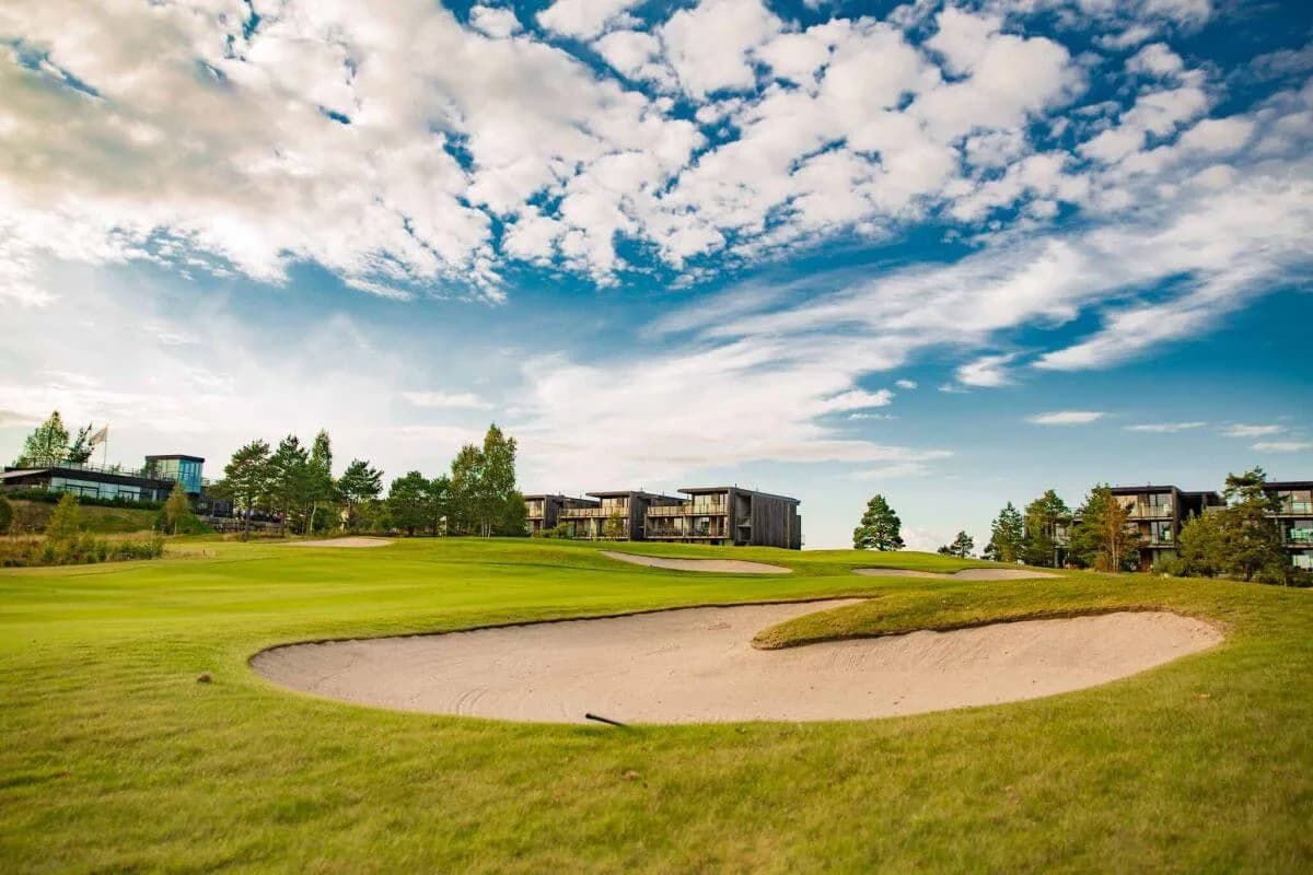 Putting green at Kragerø Golf Club with golfers and clubhouse in the background