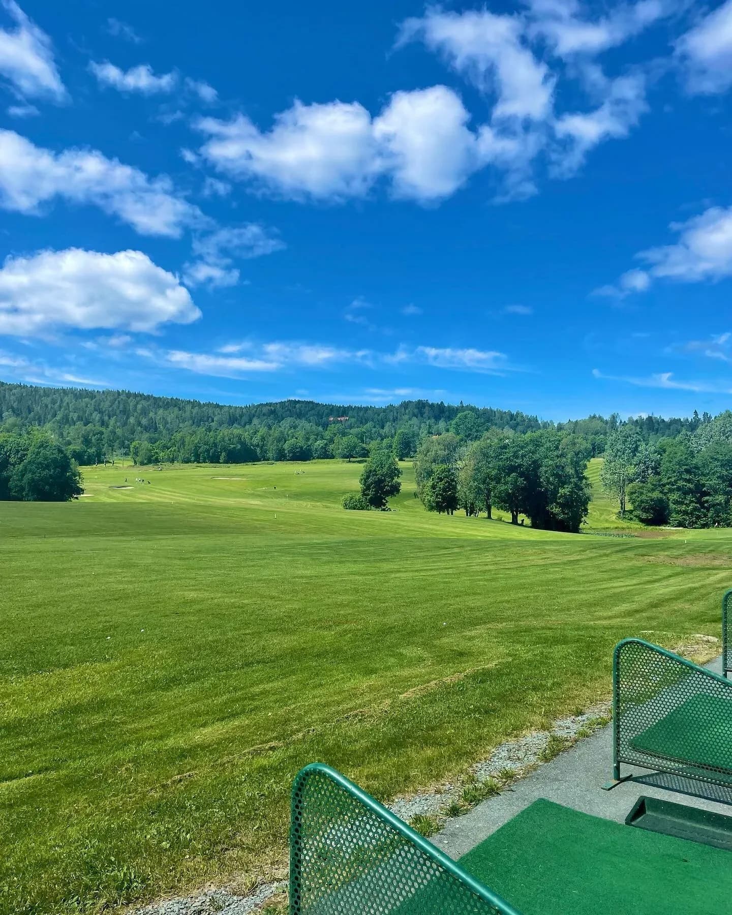 Lommedalen Golf Club with green landscape, dense forest in background and blue sky with scattered clouds