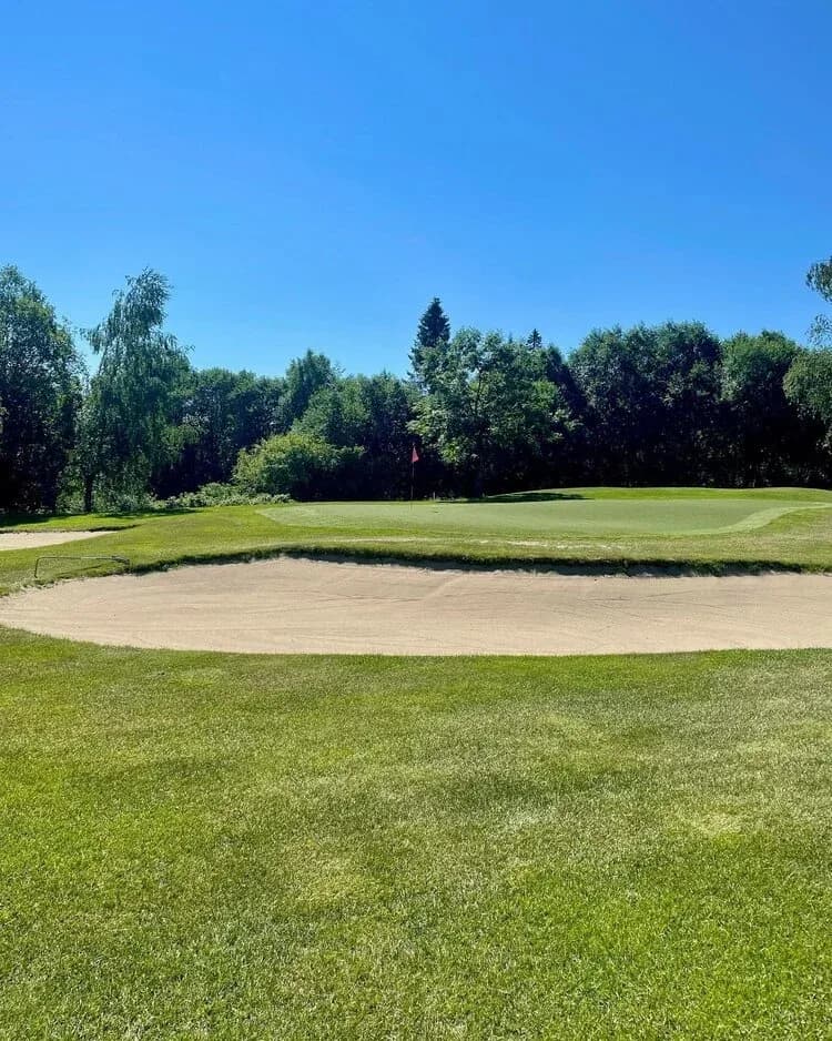 Green at Lommedalen Golf Club with sand bunker surrounded by dense forest under blue sky