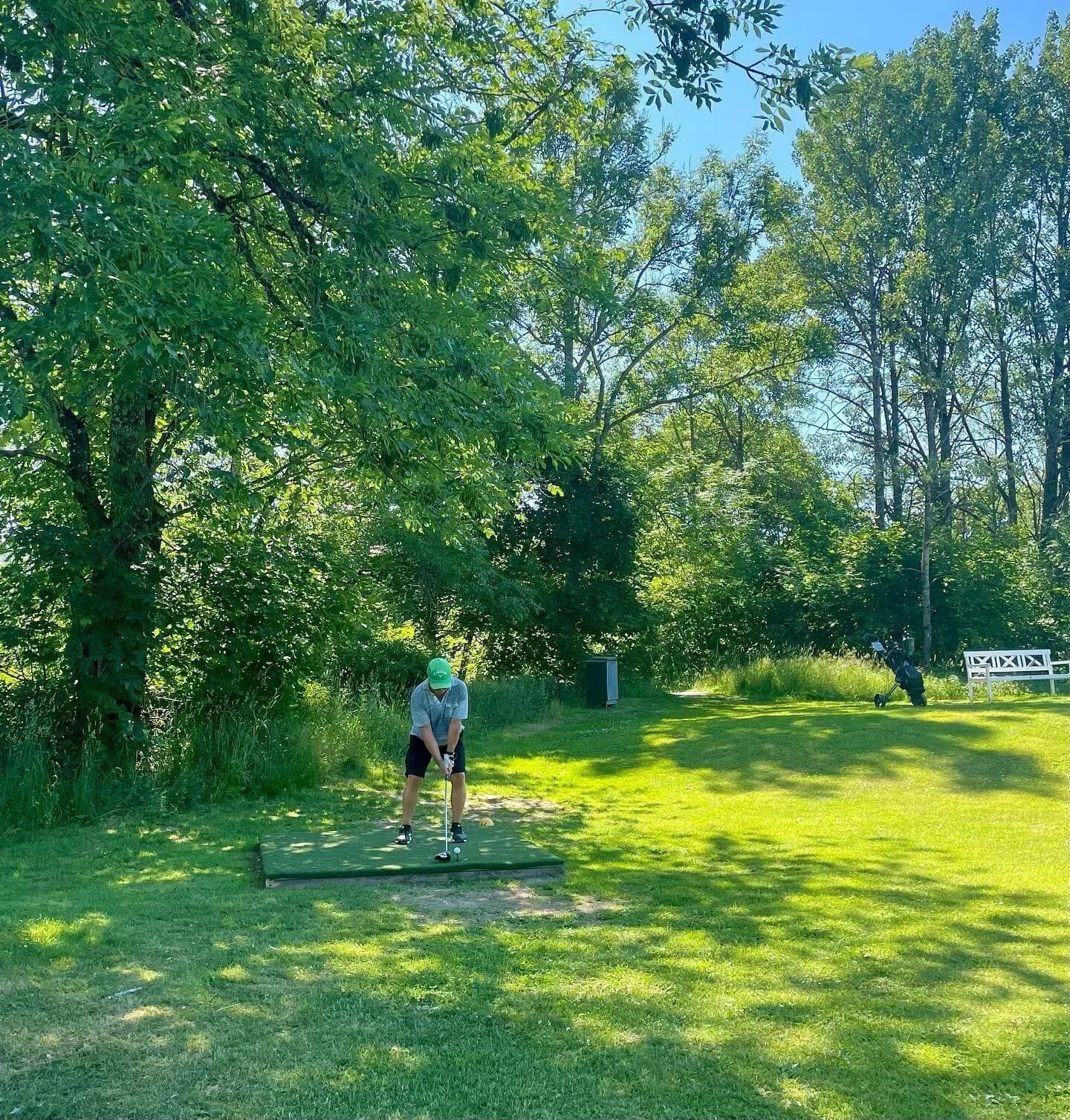 Golf player at Lommedalen Golf Club teeing off on sunny day with trees in background
