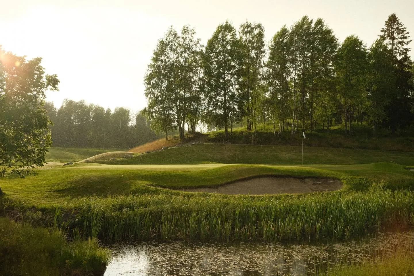 Green at Oppegård Golf Club with water hazard in foreground and dense forest in background