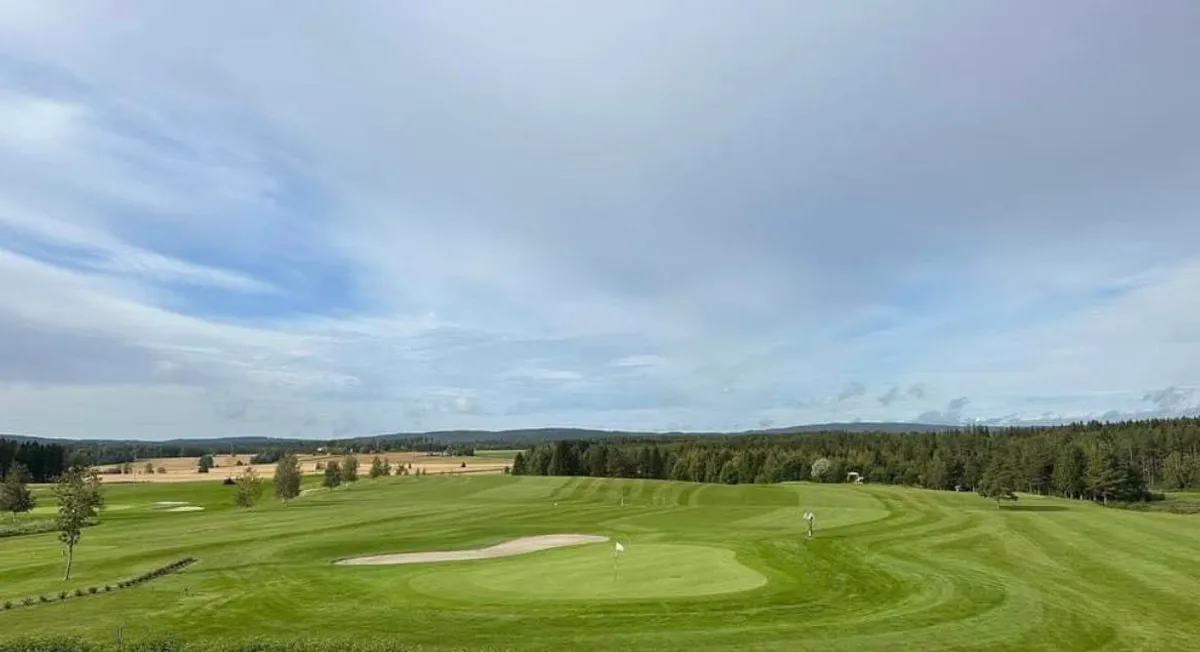 Panoramic view of green and bunkers on hole 2 at Romerike Golf Club with farmland and forest