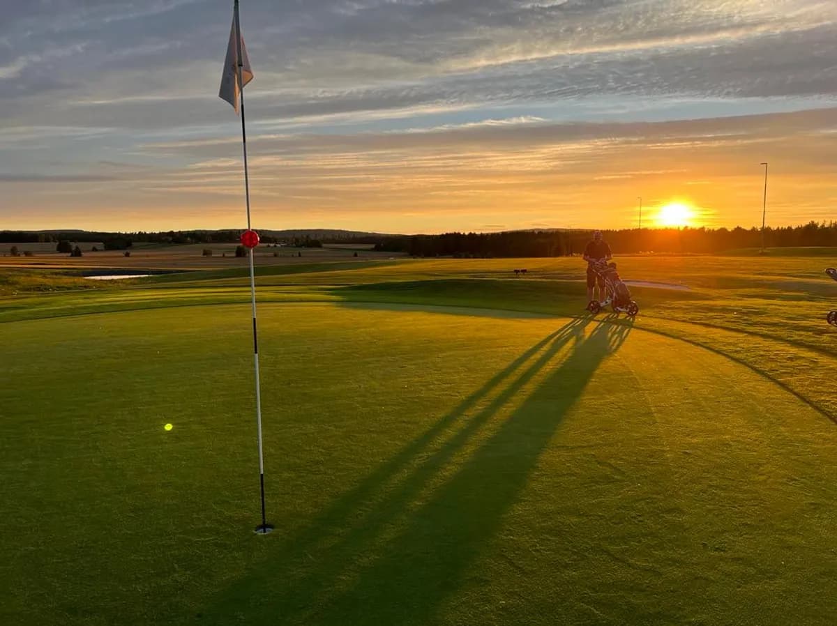 Golfer at the green on hole 8 at Romerike Golf Club at sunset with flag and long shadows