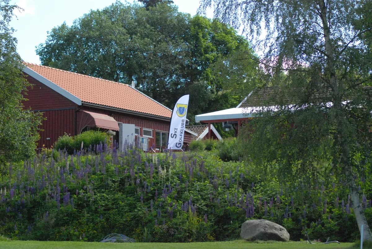 Clubhouse at Ski Golf Club with red wooden building, lupins and club banner in summer